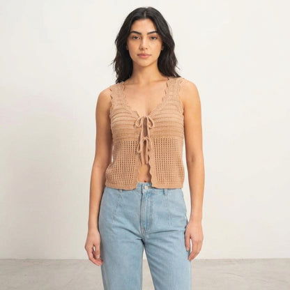 Woman in a crochet top and jeans against a neutral background.