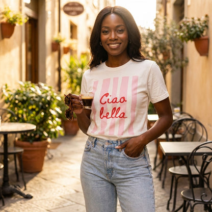 Woman in sunny alley with espresso, wearing "Ciao bella" tee.