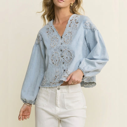 Woman in a blue embroidered blouse and white pants.