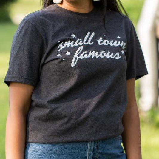 Person wearing a "small town famous" T-shirt outdoors.