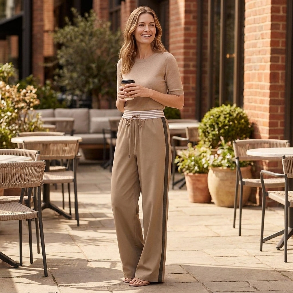 Woman in casual outfit holding a coffee in outdoor cafe setting.