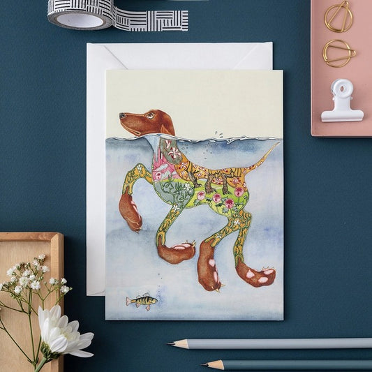 Artistic card of a floral-patterned dog swimming, surrounded by stationery items.