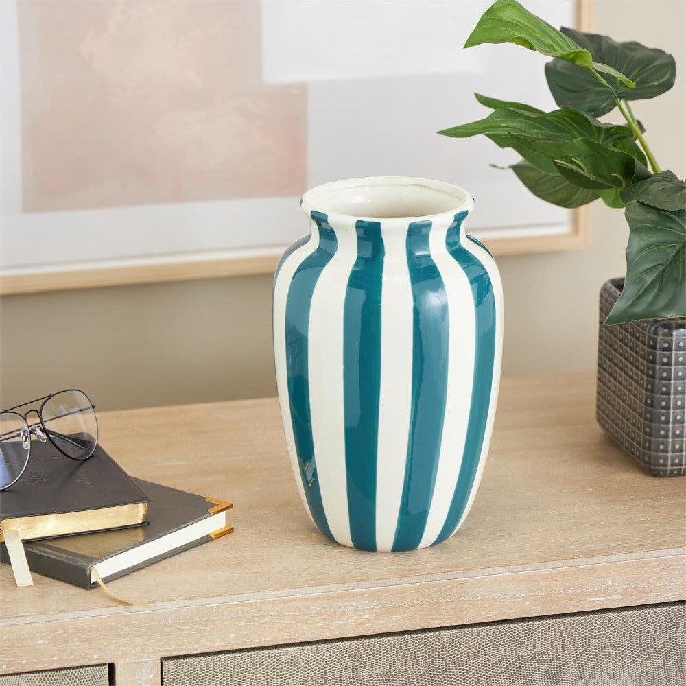 Striped vase on a wooden table with books and a potted plant.