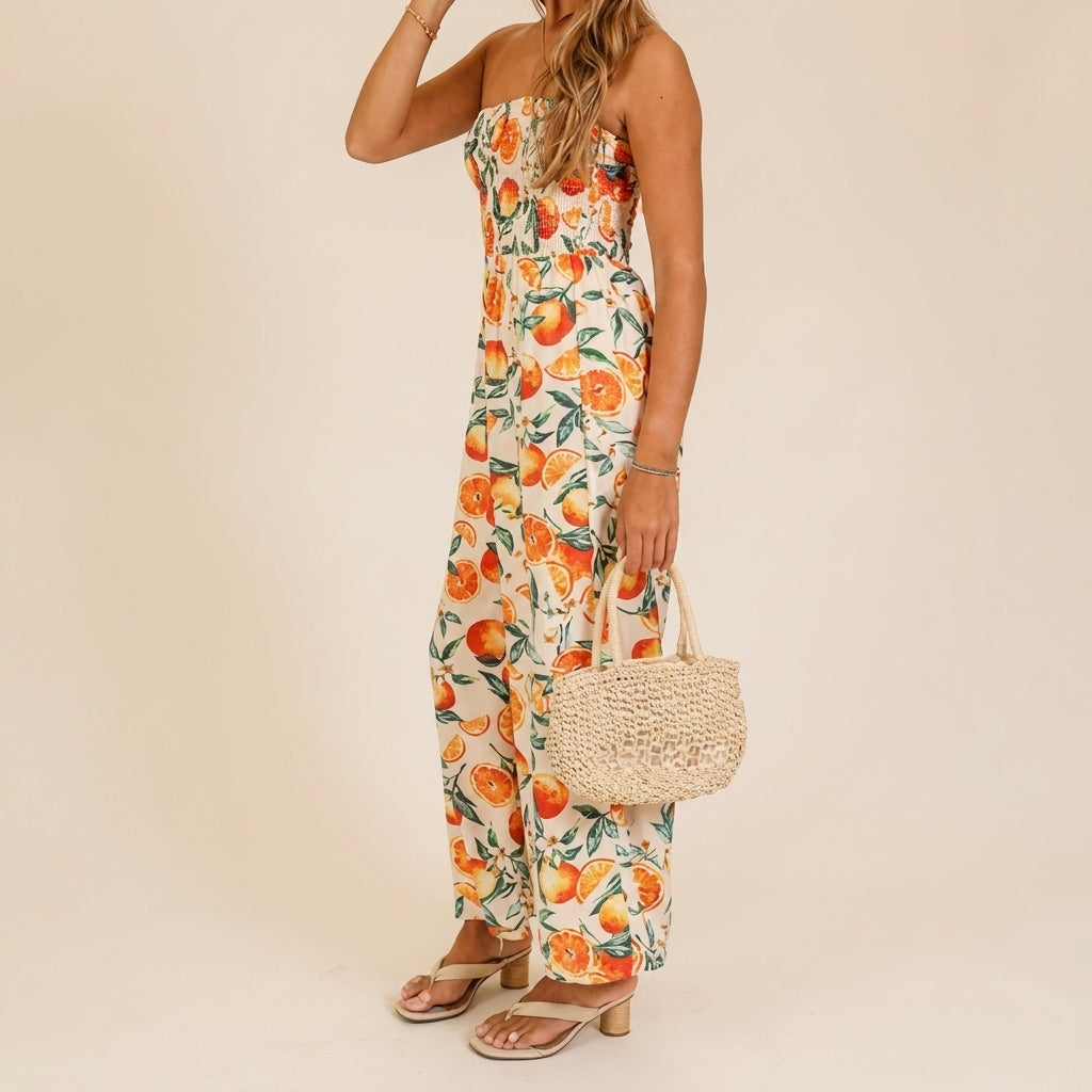 Woman in a citrus-pattern jumpsuit holding a woven bag.