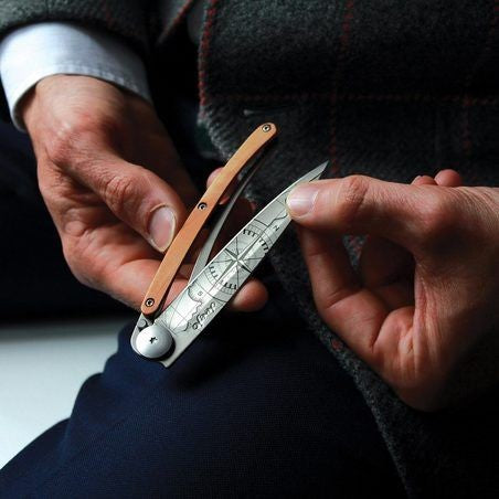 Hands holding an ornate, engraved folding blade with a wooden handle.