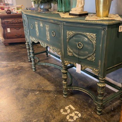 An ornate teal vintage sideboard with gold accents and carved details displayed in a furniture shop.