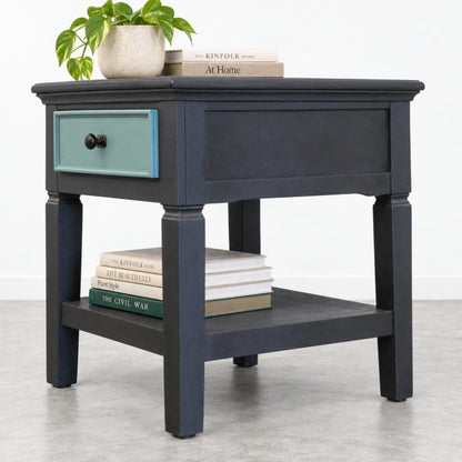 Dark end table with books, drawer, and a potted plant on top.