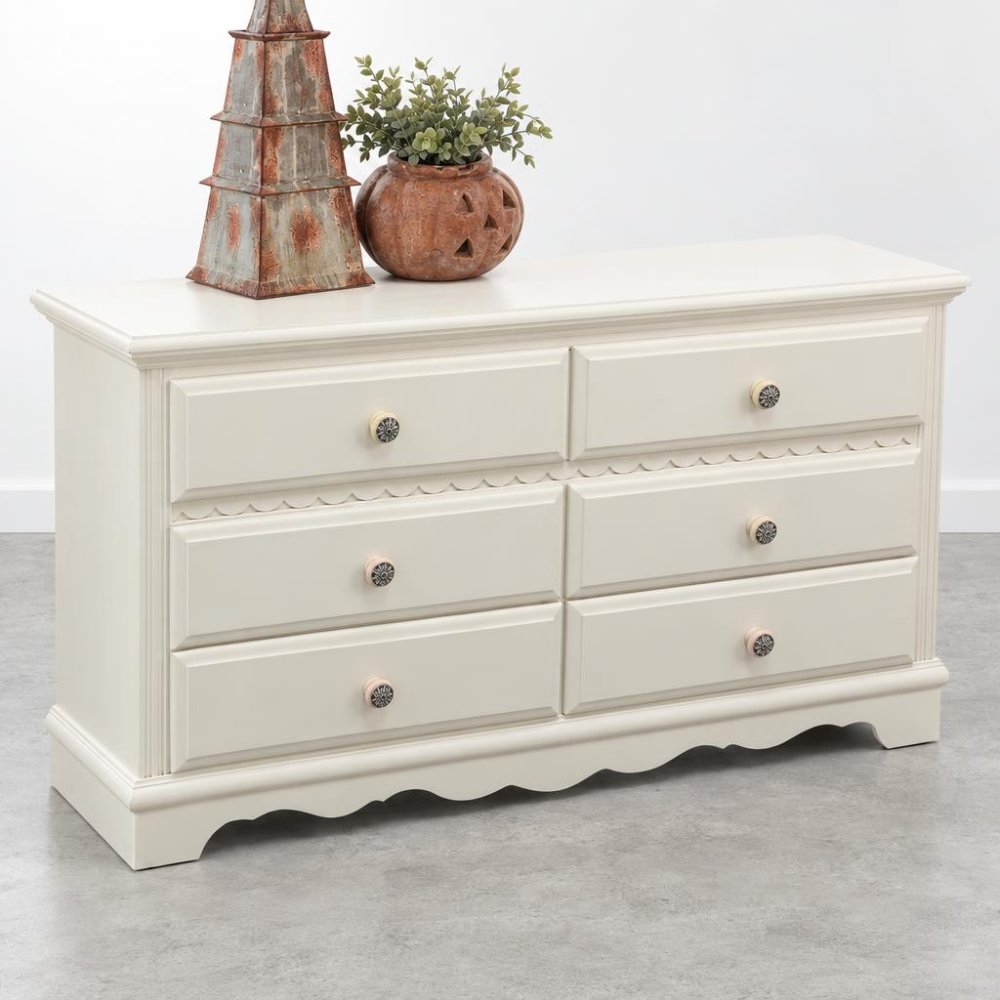Cream dresser with six drawers, topped with rustic decor and a plant.