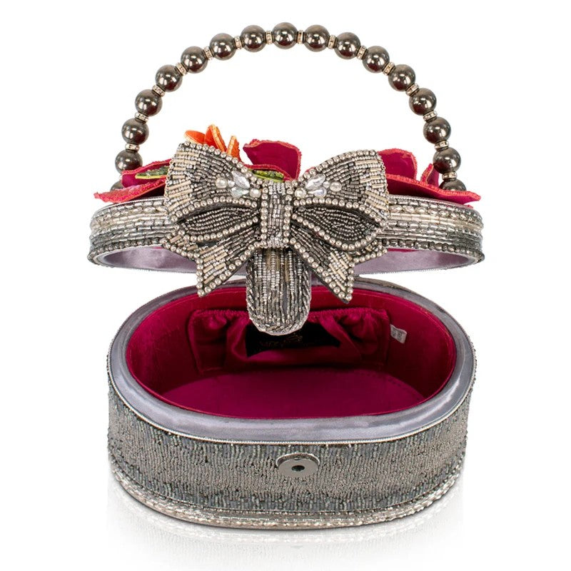Beaded clutch with bow, floral accents, and metallic handle, open to reveal red interior.
