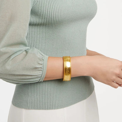Close-up of a person wearing a wide gold cuff bracelet with a sage green sweater.