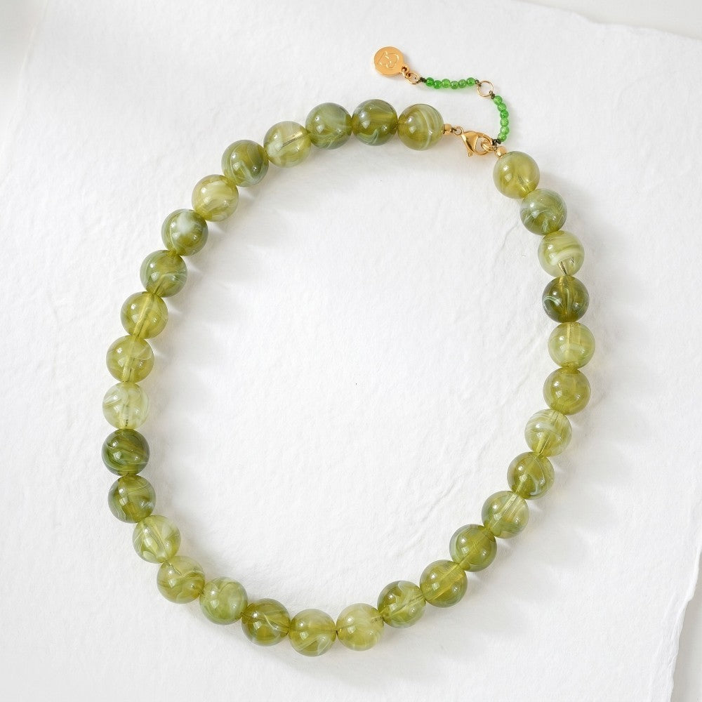 Green beaded necklace with small gold charm and green clasp on a white background.