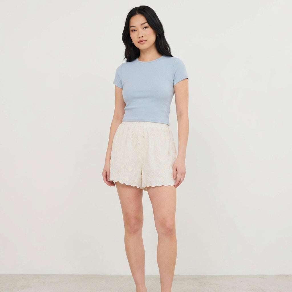 Woman in blue top and white shorts on plain background.