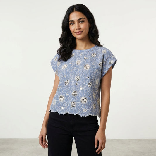 Woman in floral blue top and black pants, standing confidently indoors.