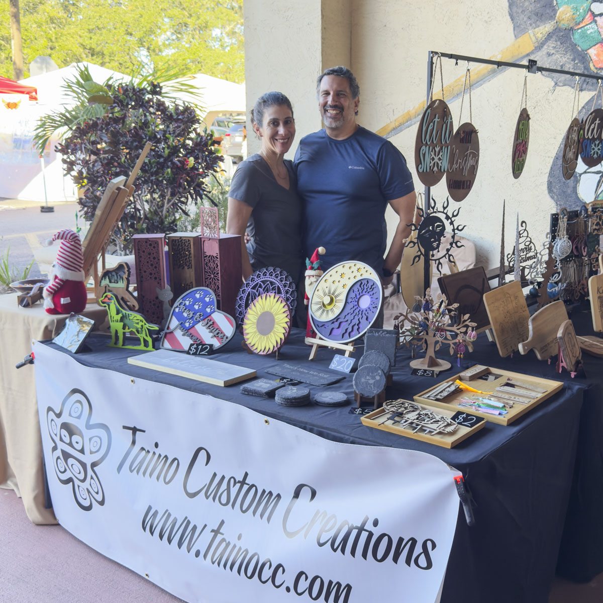 Two vendors behind a table of hand-painted plates and jewelry